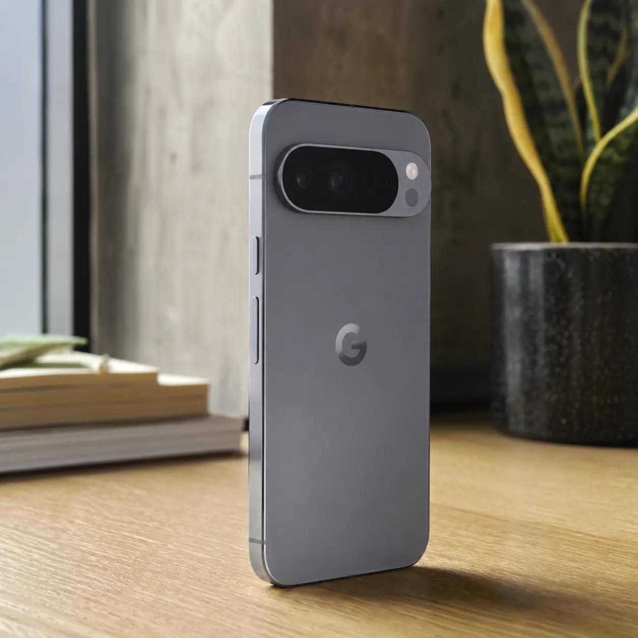 Teléfono inteligente Google Pixel gris de pie sobre un escritorio junto a una ventana iluminada
